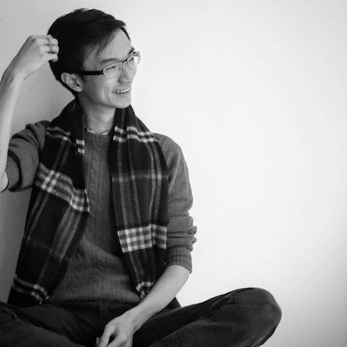 Black-and-white photo of George smiling while sitting cross legged and brushing his
hair